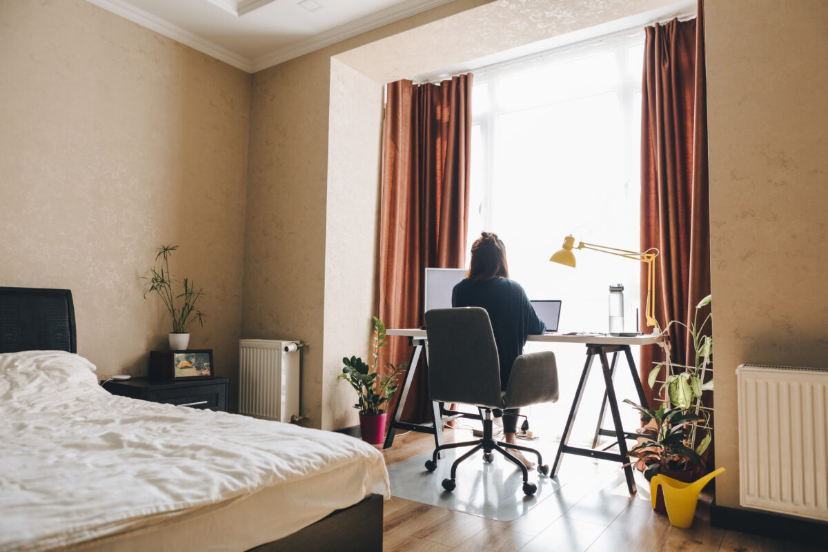 A woman works on her laptop at a desk in her bedroom