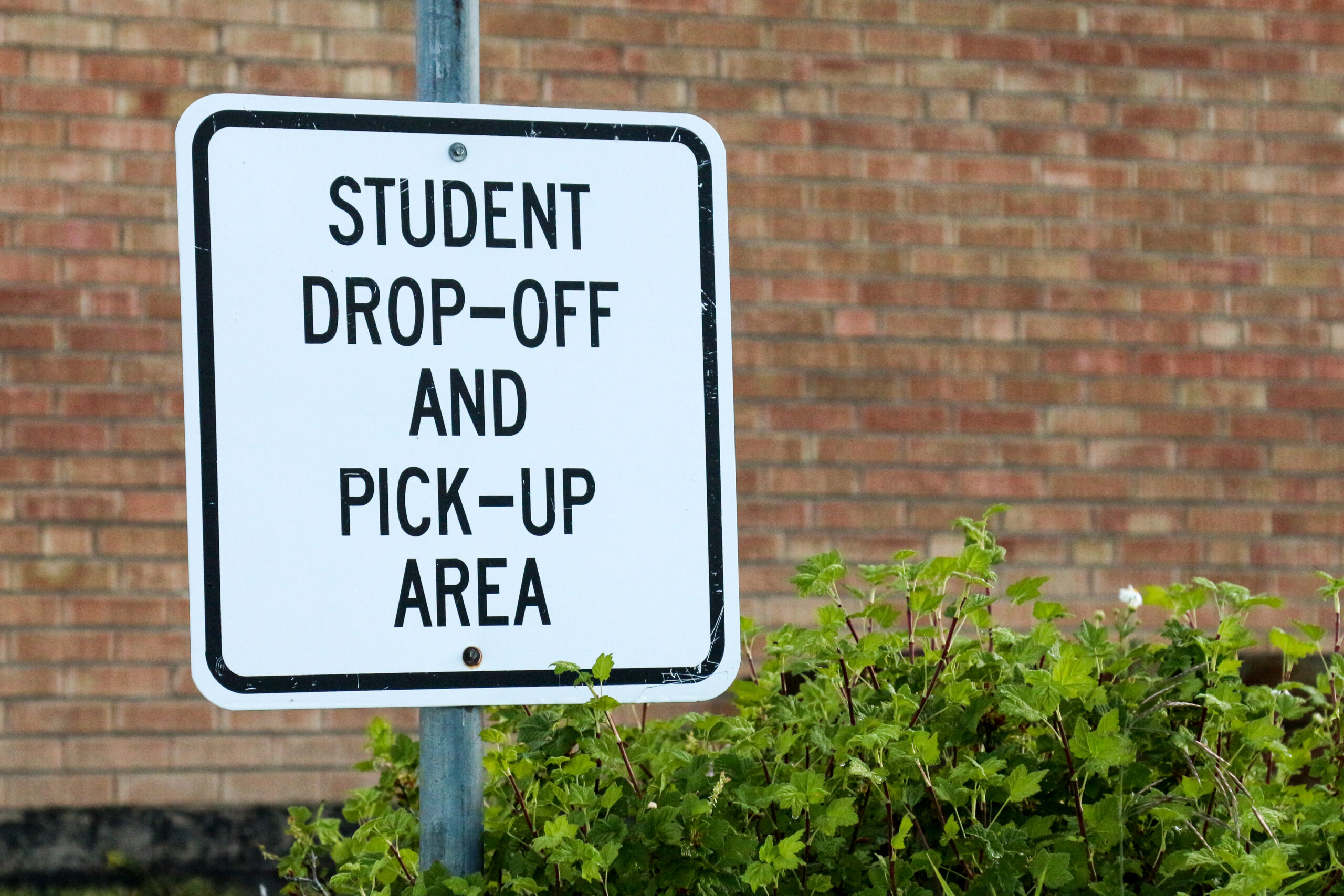 Sign for Student Drop off and Pick Up Area against brick school