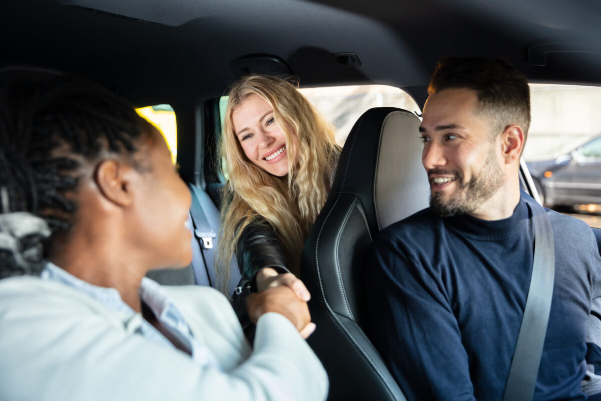 Three coworkers smiling and shaking hands while carpooling together to work